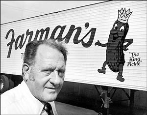 Farman in front of a semi trailer reading Farman's, The King Pickle, with an illustration of an anthropomorphic pickle smiling and wearing a crown